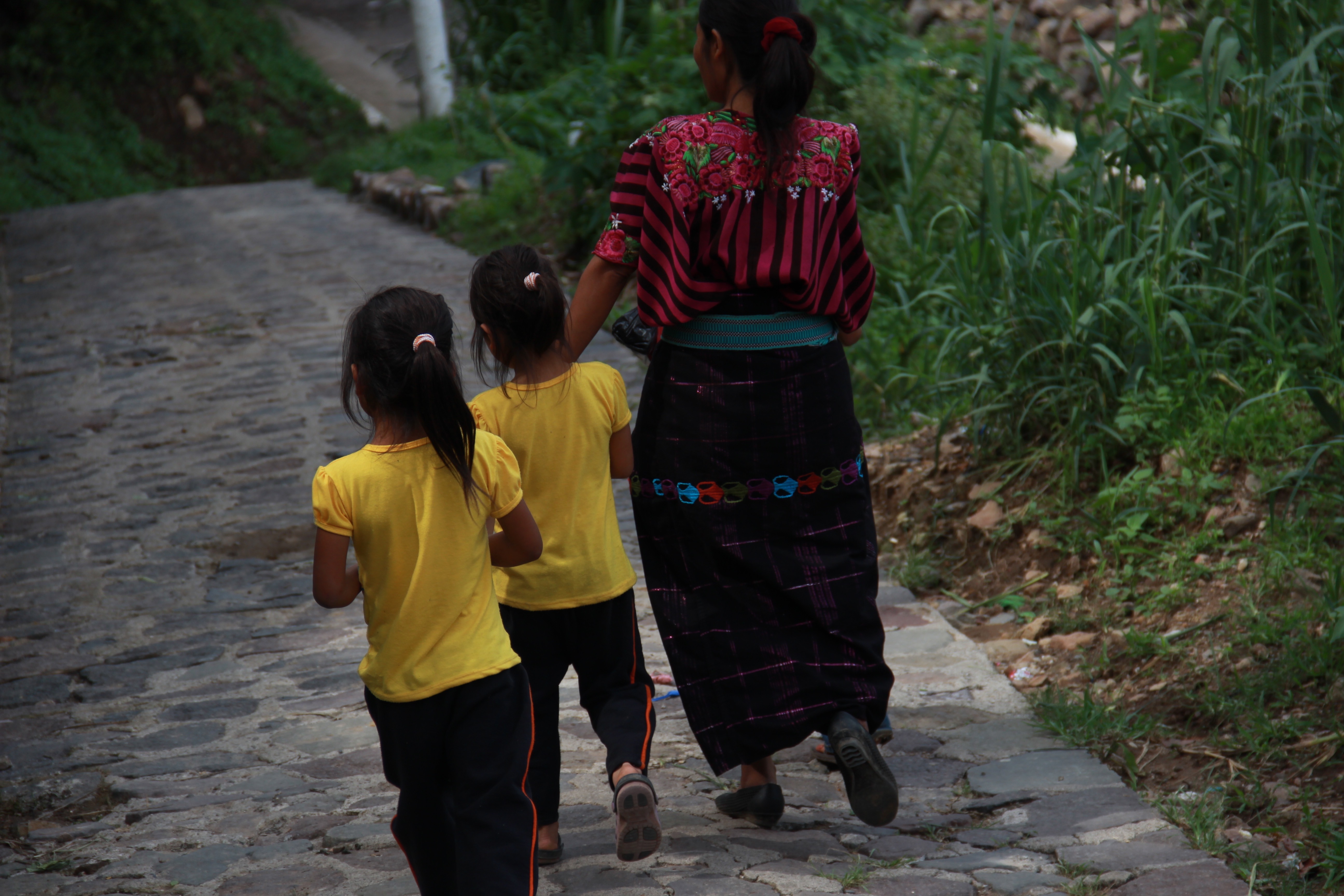 Madre guatemalteca caminando con dos niñas en traje típico