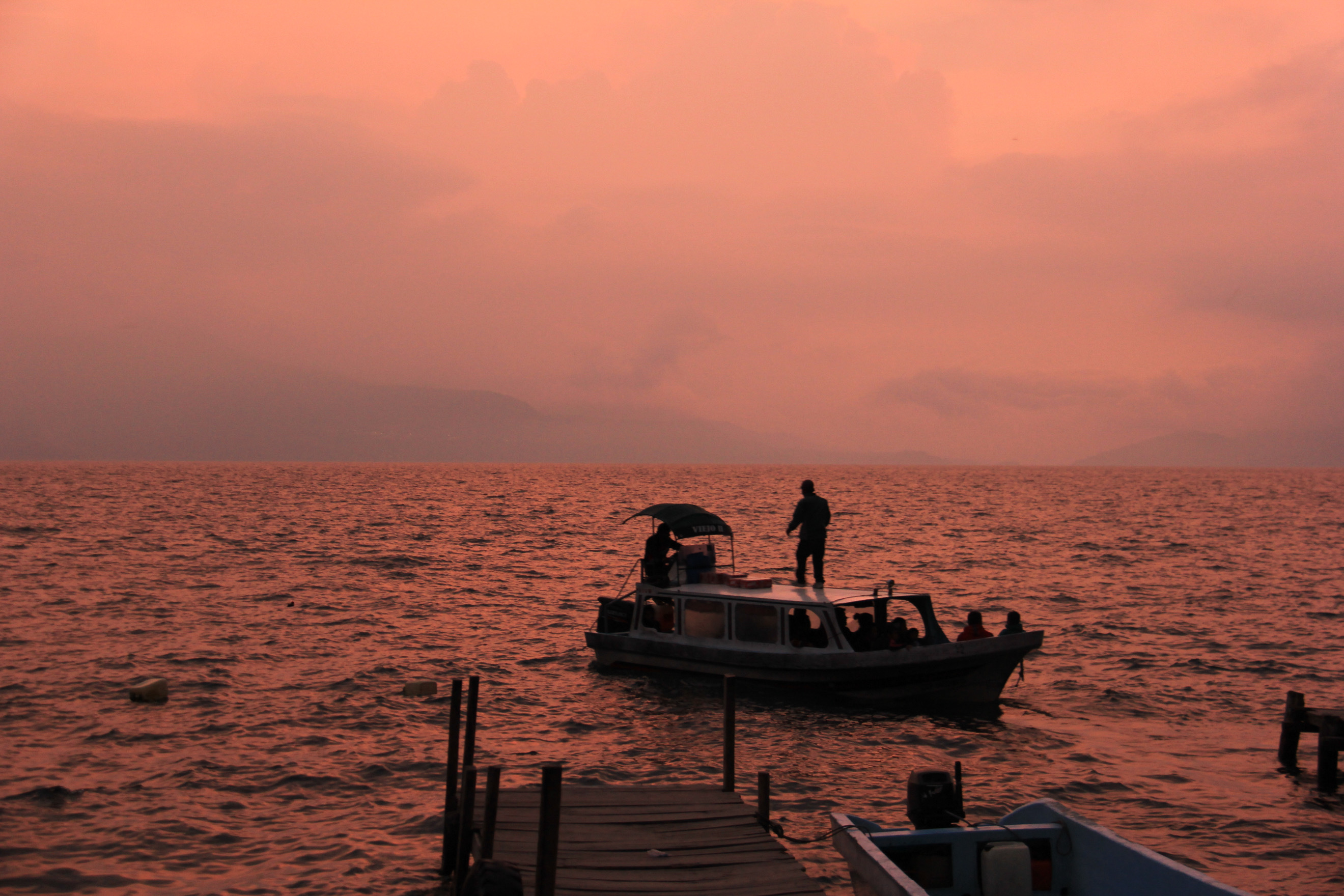 Atardecer en el Lago de Atitlán con una lancha y personas navegando