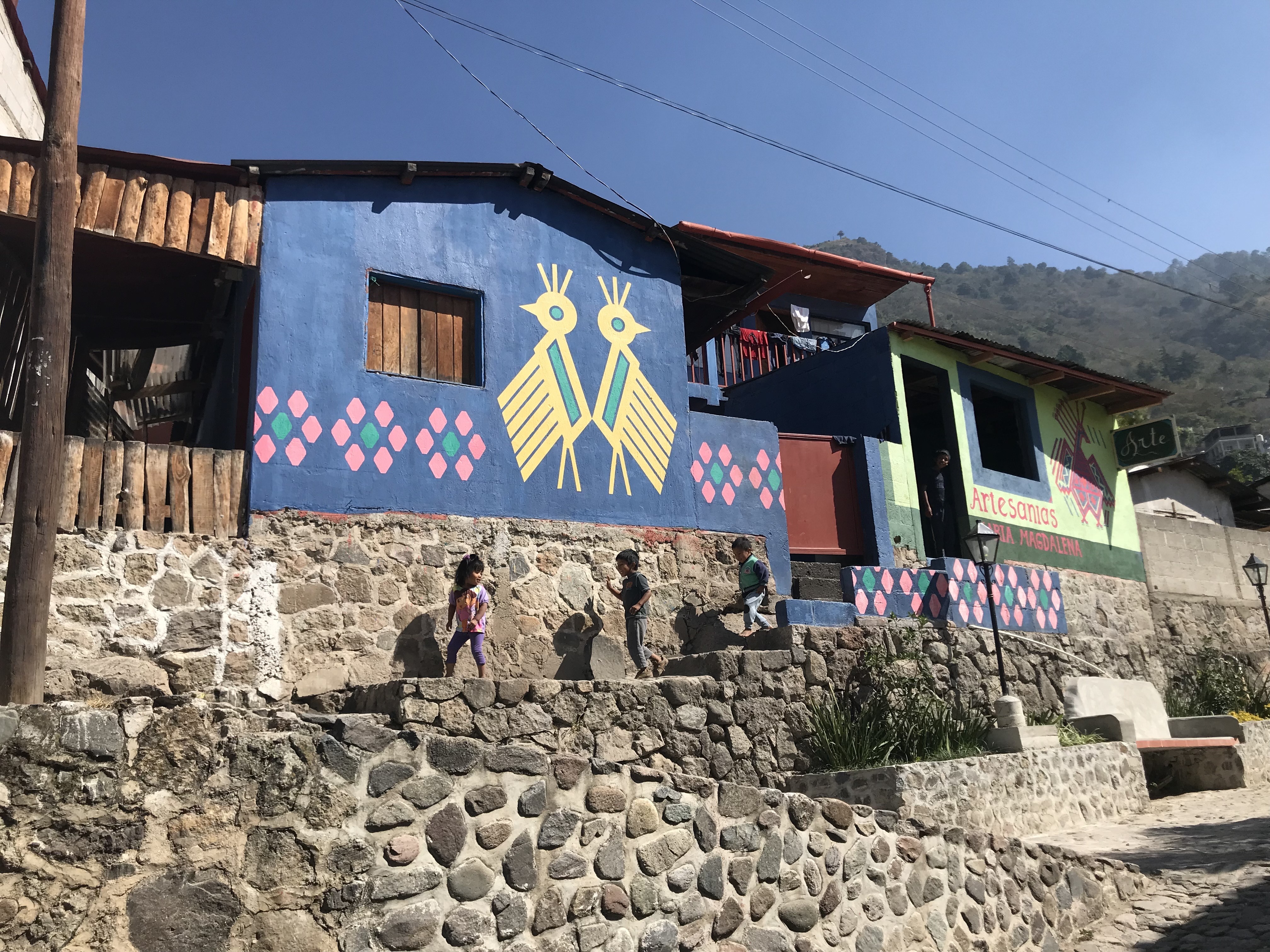 Niños guatemaltecos frente a un mural azul con pájaros pintados